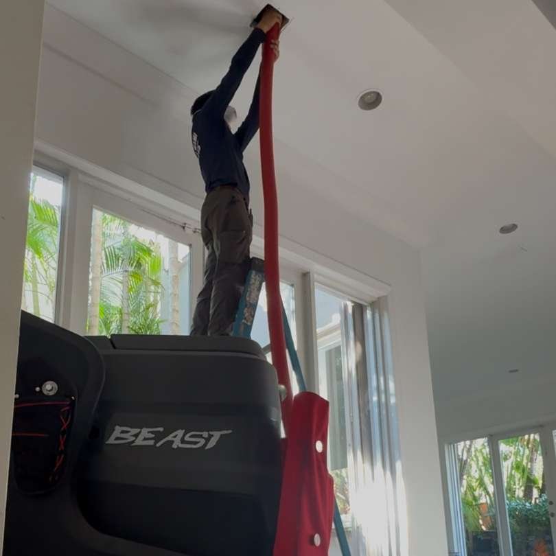 Technician performing air duct and coil cleaning in a Miami home using a high-powered vacuum system to improve indoor air quality.
