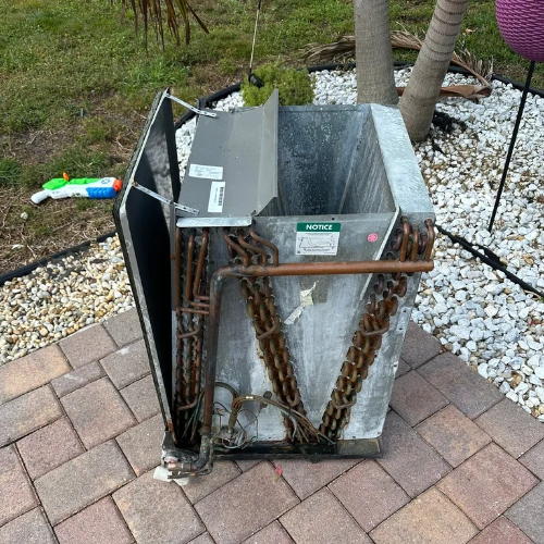 An open HVAC evaporator coil pulled out on a paver patio for a deep technical inspection during an AC maintenance tune-up in Fort Lauderdale.