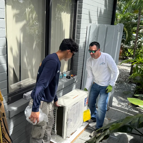 Two HVAC technicians installing a coastal-grade mini-split air conditioner condenser outside a residence in Fort Lauderdale.